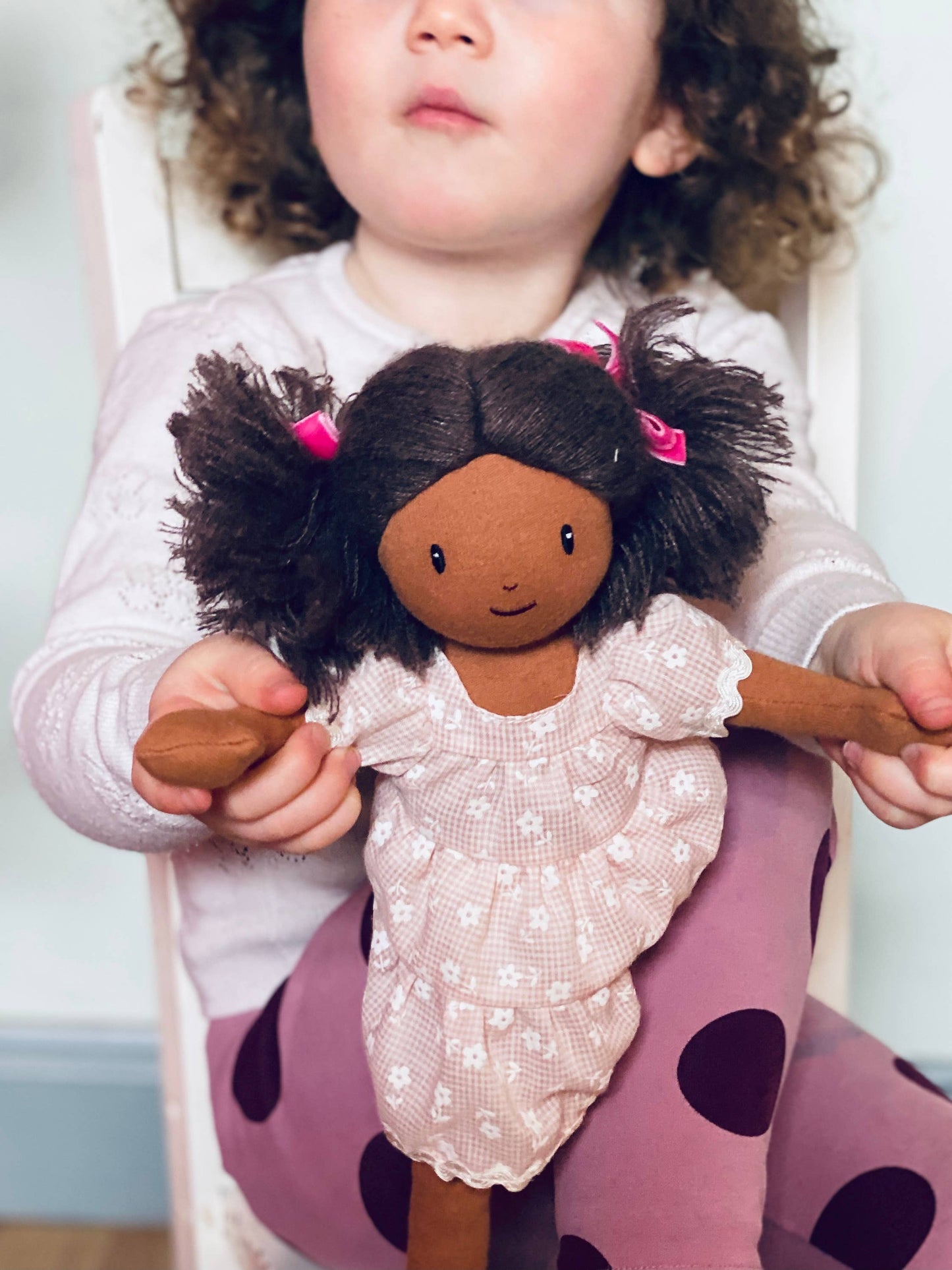 Child holding a doll with dark hair and pink bows, sitting on a purple chair.