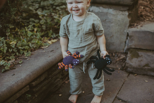 Child holding two spiders, one is black and the other purple and orange
