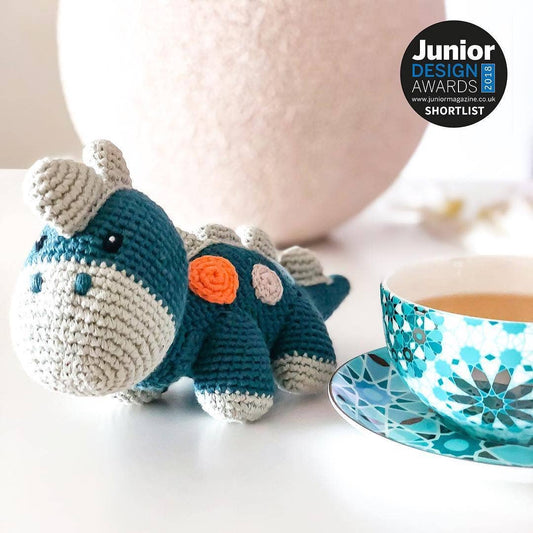 A crochet dinosaur pull-along toy in petrol blue with a rattle, on a wooden cart, with a natural cotton pull-string.