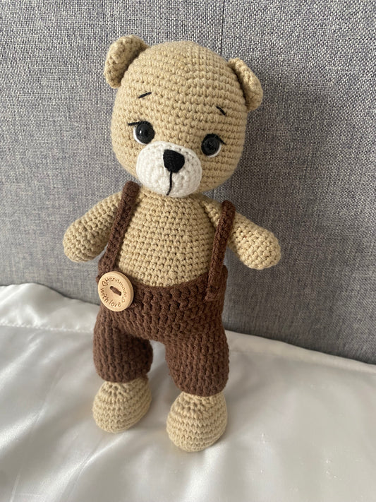 Crocheted teddy bear with a brown outfit on a textured surface