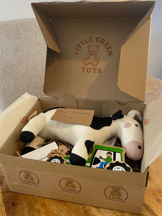 Open cardboard box with a plush cow toy and Little Green Tots branding.