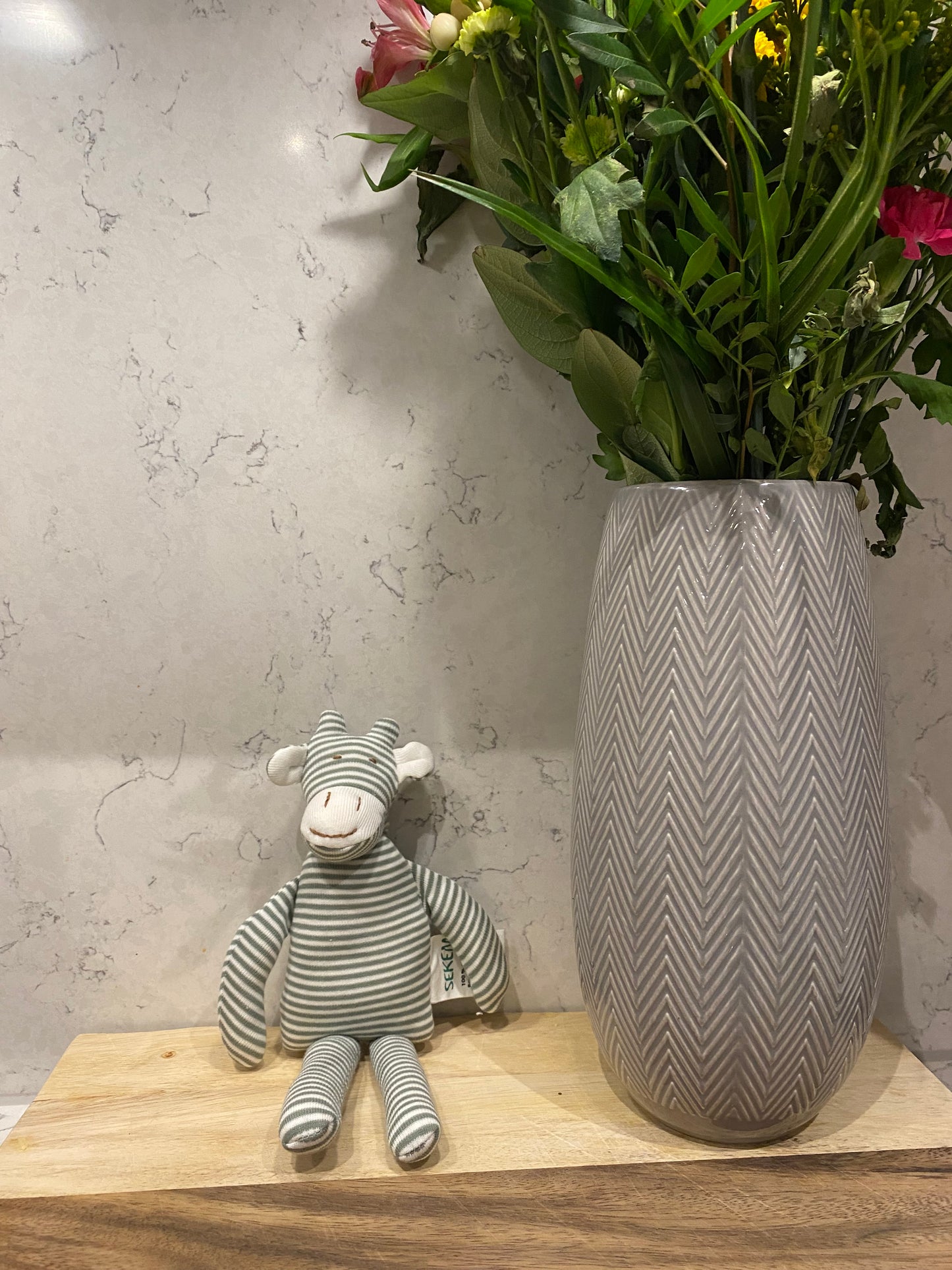 Gray striped giraffe toy on a wooden surface with flowers in the background
