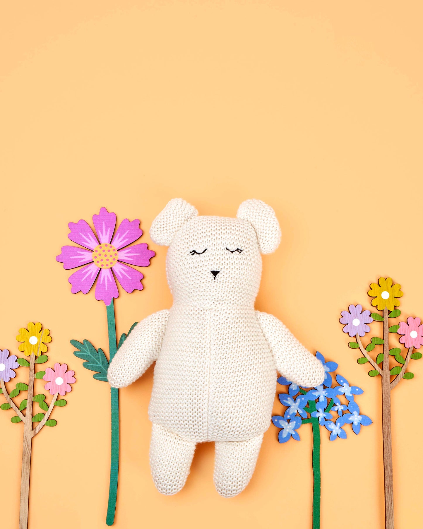 White teddy bear with closed eyes surrounded by colorful flowers on a yellow background