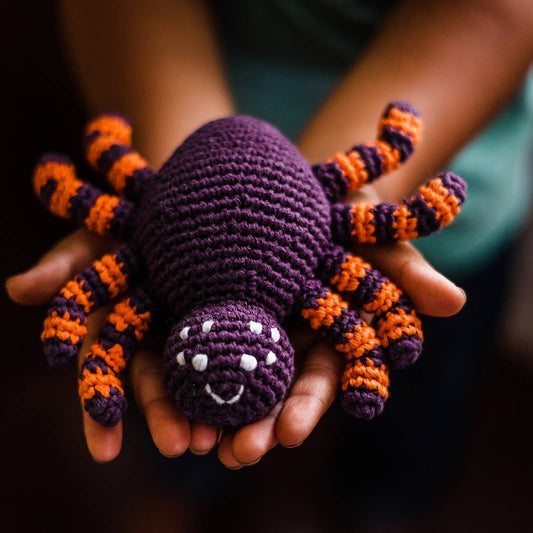 A crochet baby toy spider rattle made of purple and orange yarn with a rattle feature.
