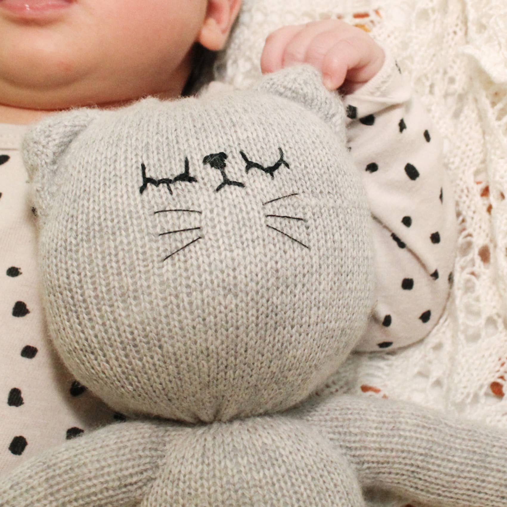 Baby holding a gray knitted cat toy with black details