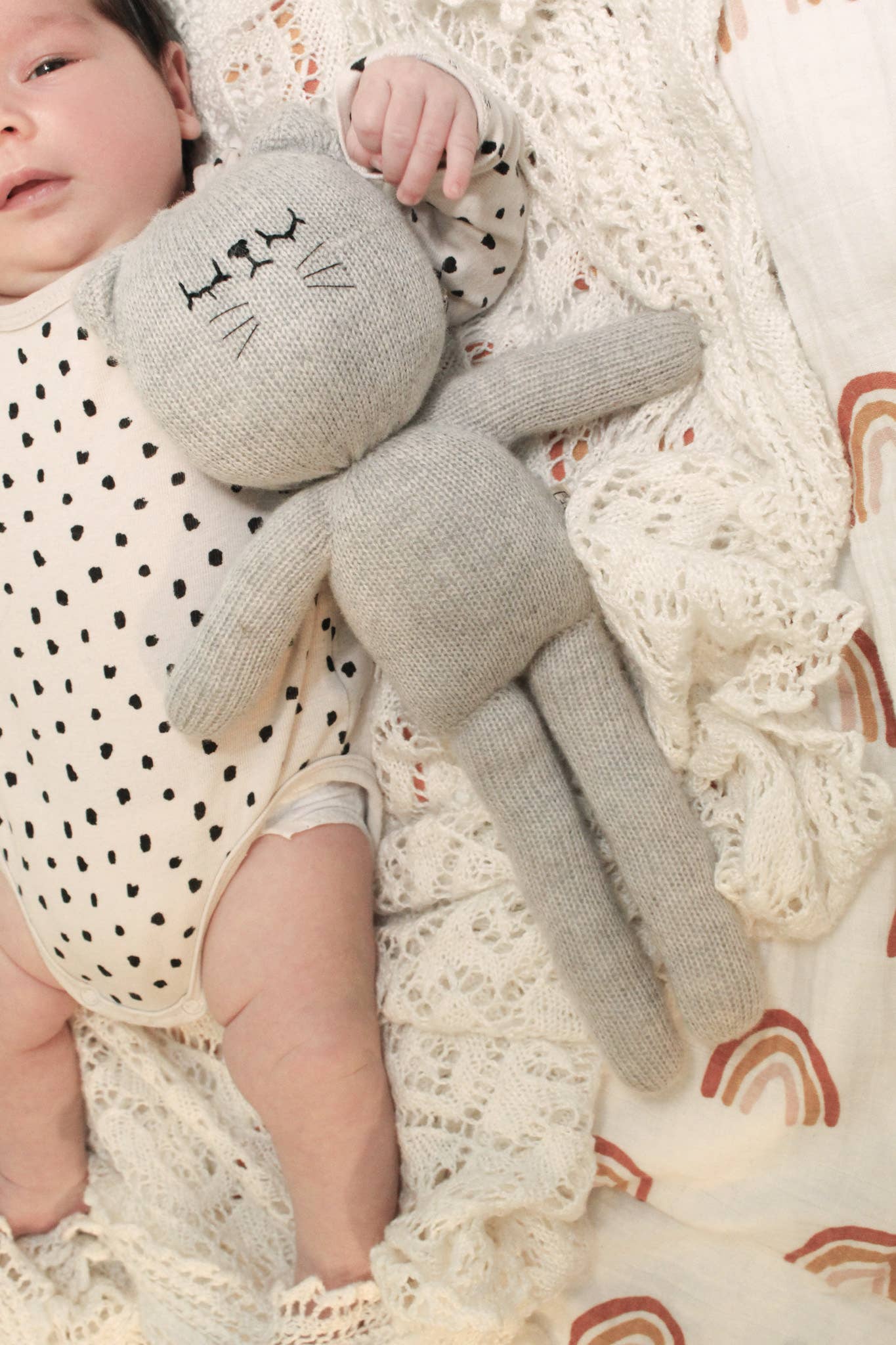 Child holding a gray knit bunny toy on a textured blanket with rainbow patterns