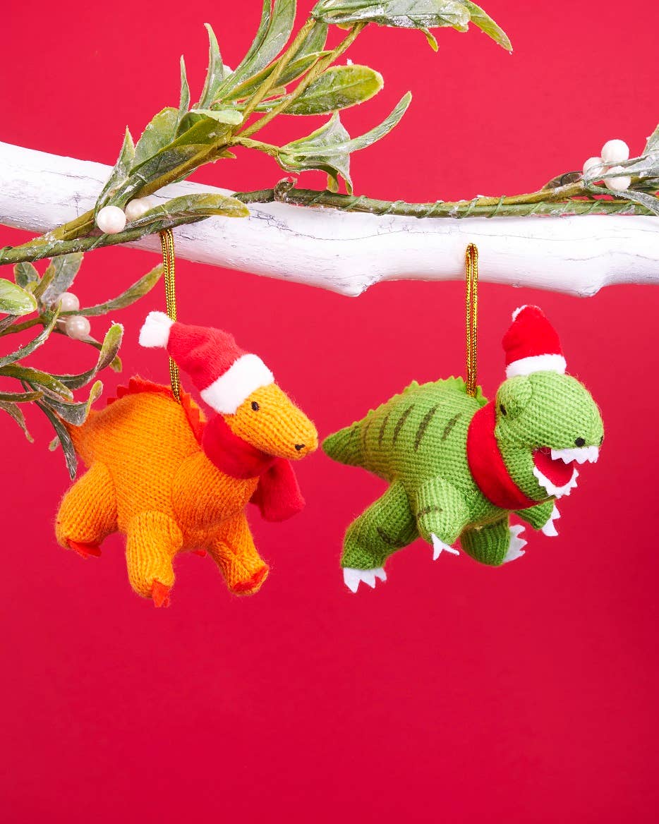 Two knitted dinosaur ornaments with Santa hats hanging from a branch against a red background.