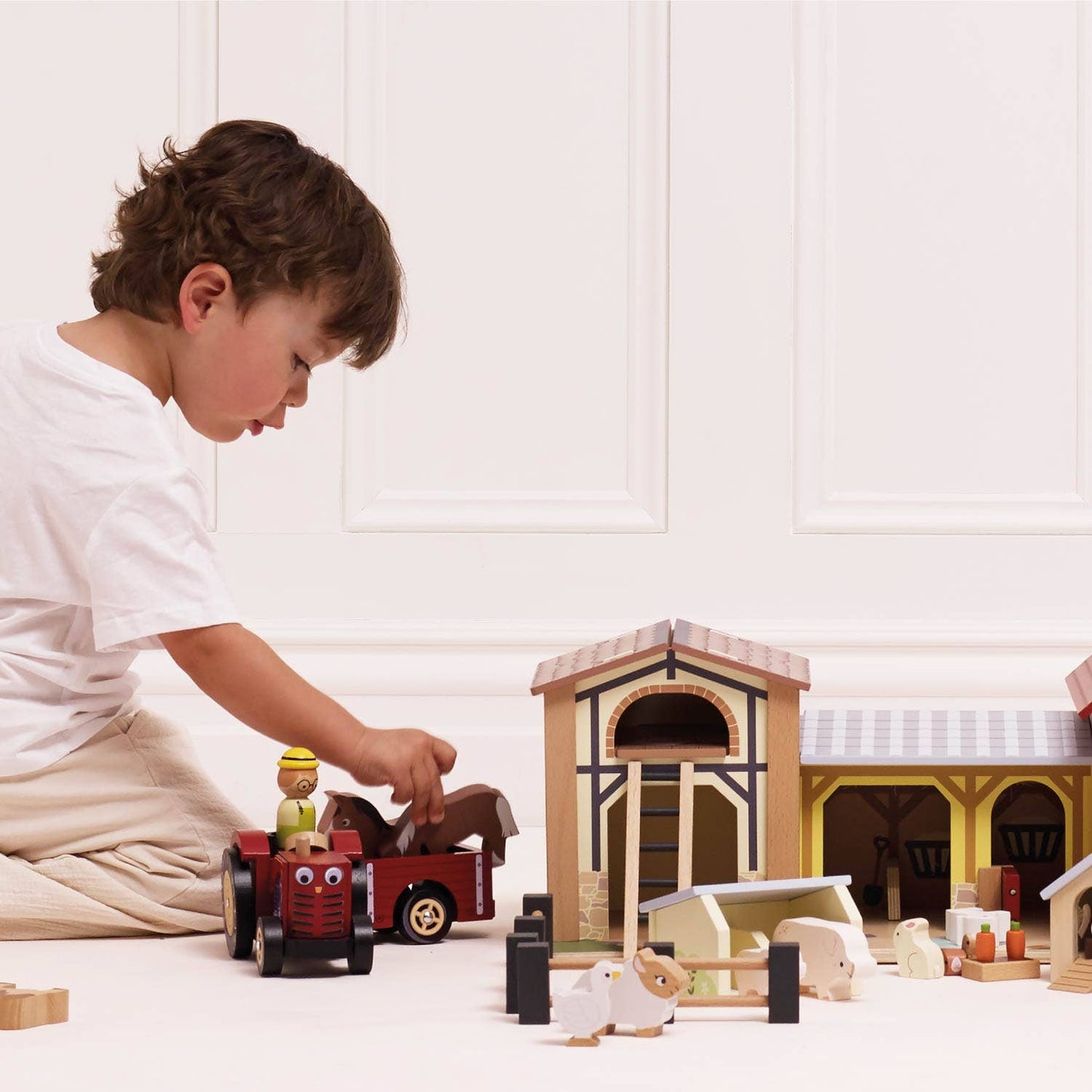 Child playing with toy farm set on a white floor.