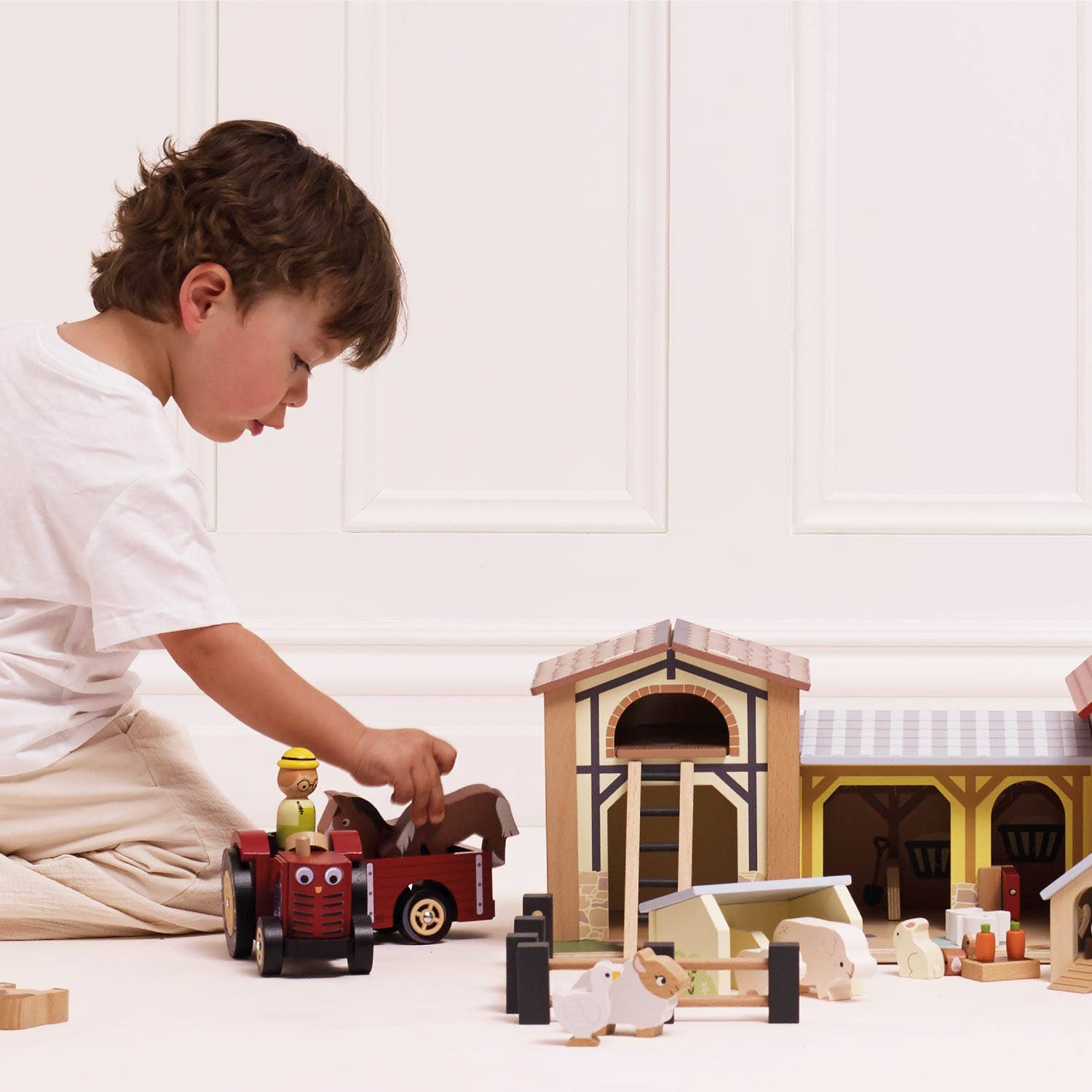 Child playing with toy farm set on a white floor.