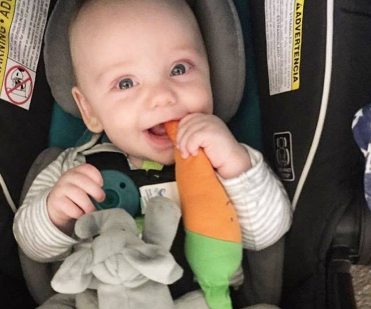 Baby in a car seat holding a toy carrot