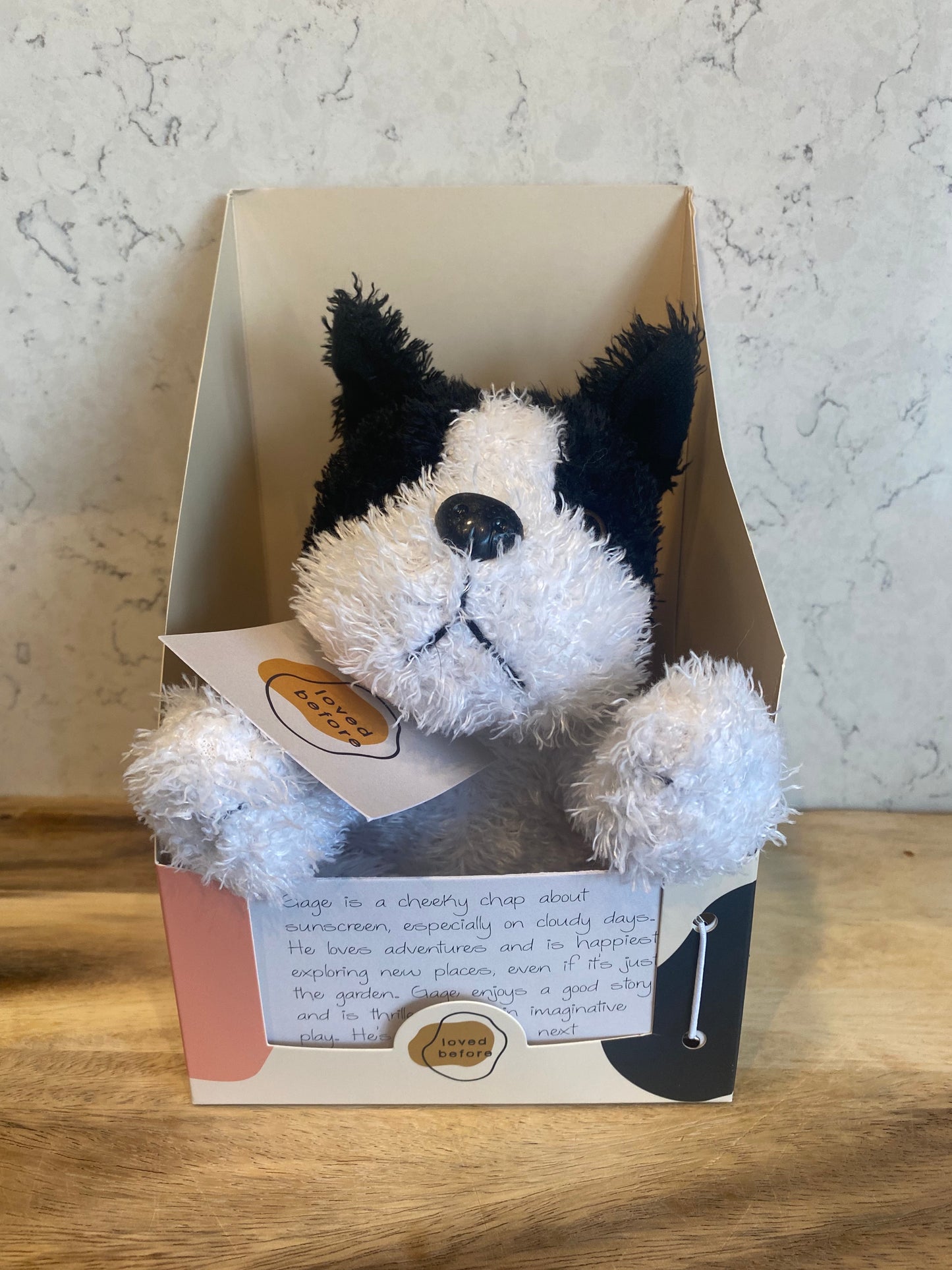 Stuffed dog toy with black and white fur in a box on a marble surface