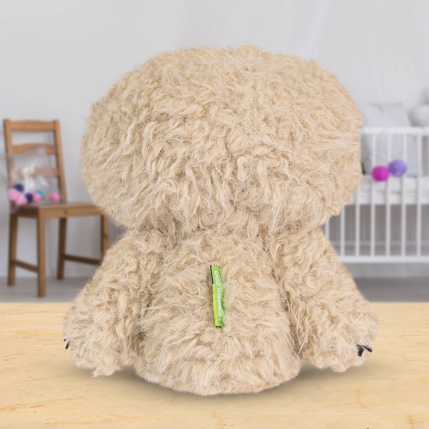 Back of sloth toy with a green tag on a wooden surface, blurred background