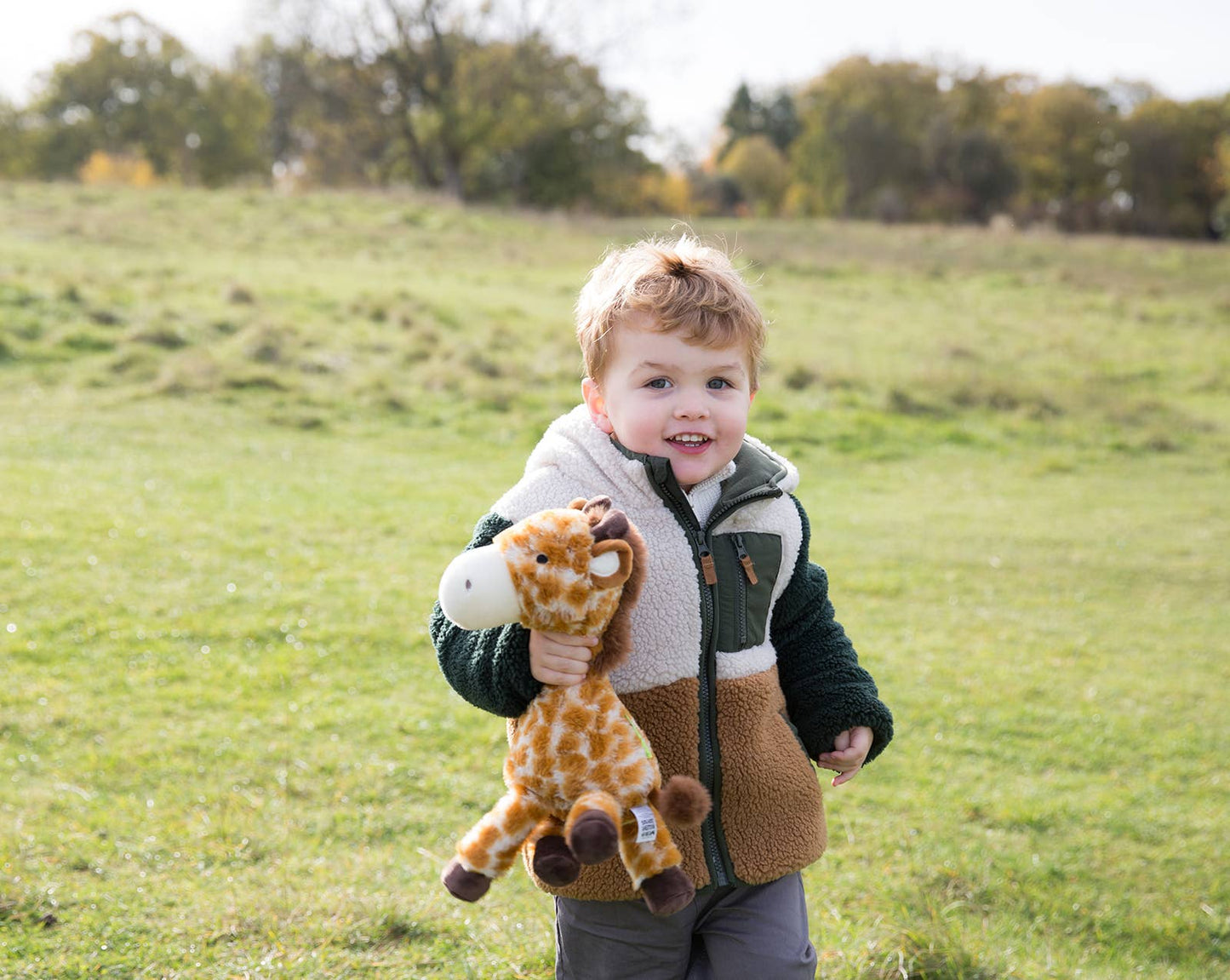 Child holding a giraffe plush toy in an open field