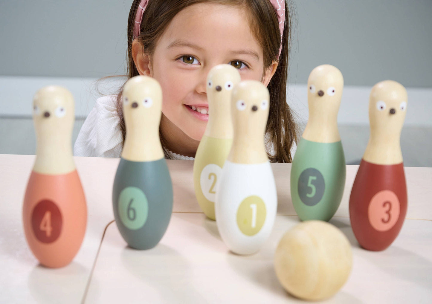 Child with wooden bowling pins and a ball on a light surface