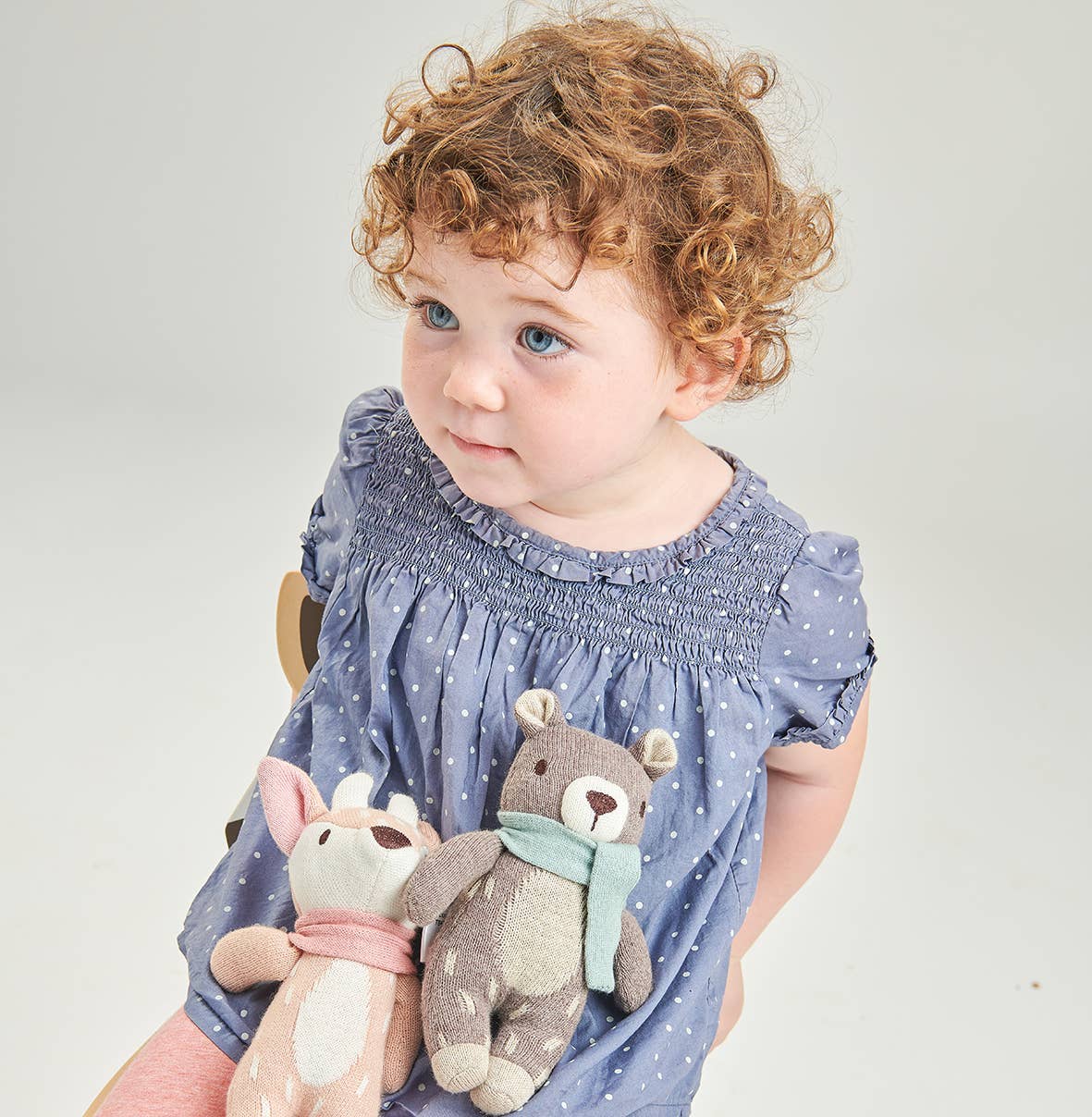 Child holding two stuffed animals against a plain background