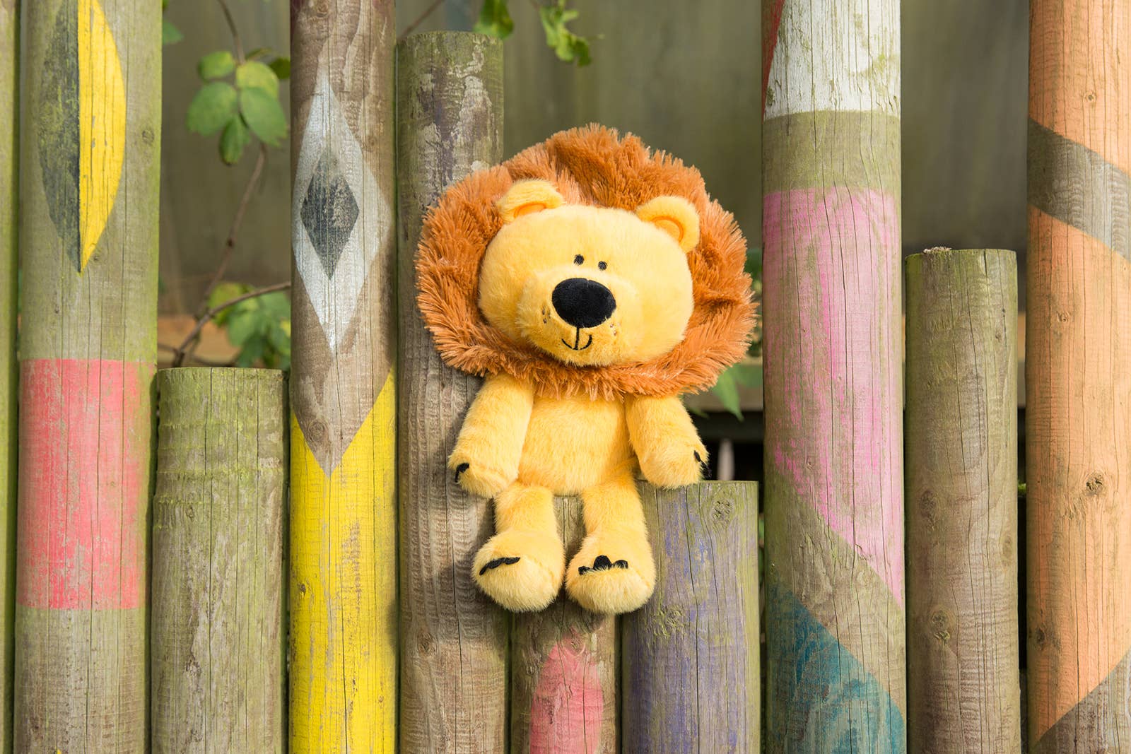 Plush lion toy on a wooden fence with colorful paint designs