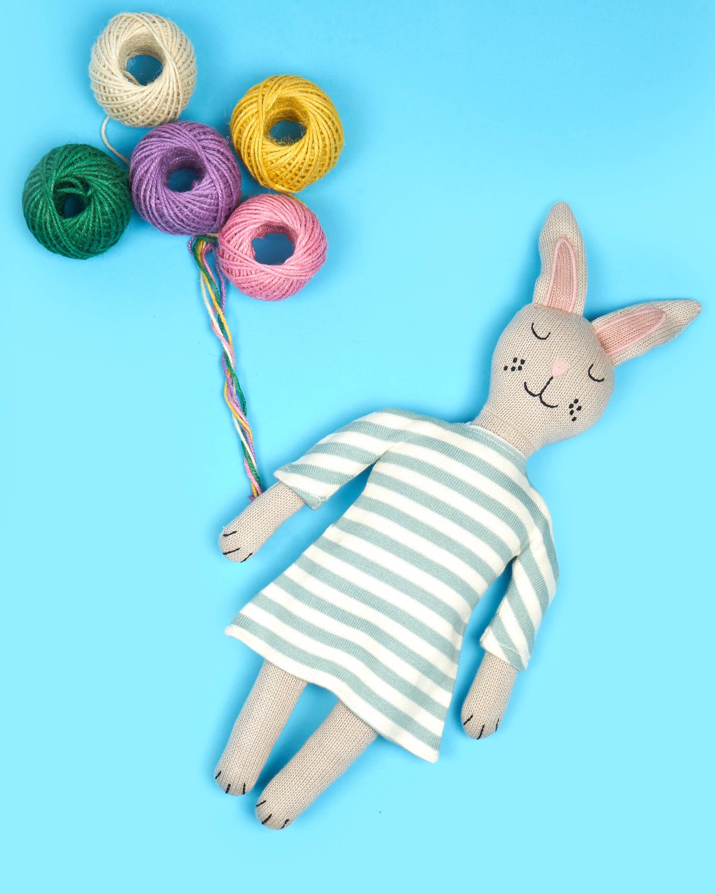 Toy rabbit in a striped dress with colorful yarn balls on a blue background