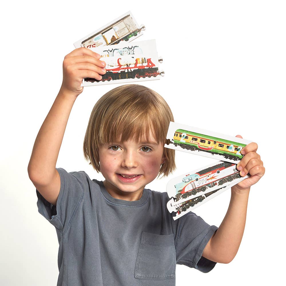 Child holding up toy train models against a white background