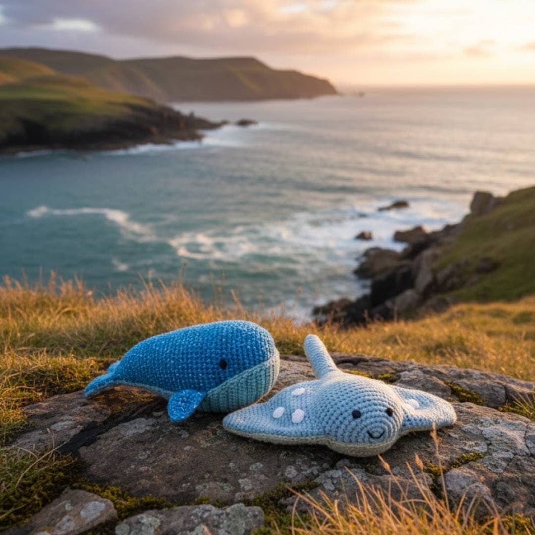 Two crochet toys on a rock with a scenic ocean view at sunset.