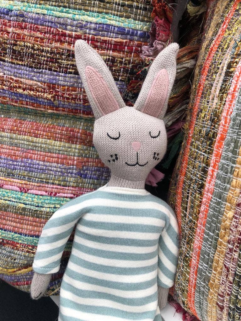 Knitted rabbit toy with striped sweater against a textured fabric background