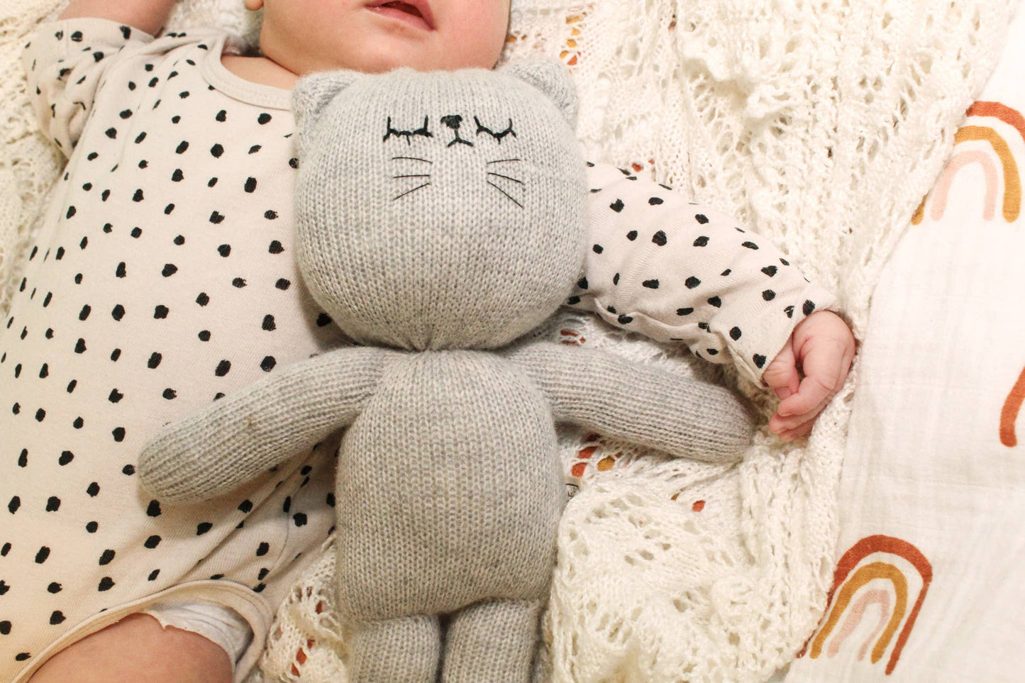 Baby holding a gray knit cat toy with black details on a soft textured blanket.