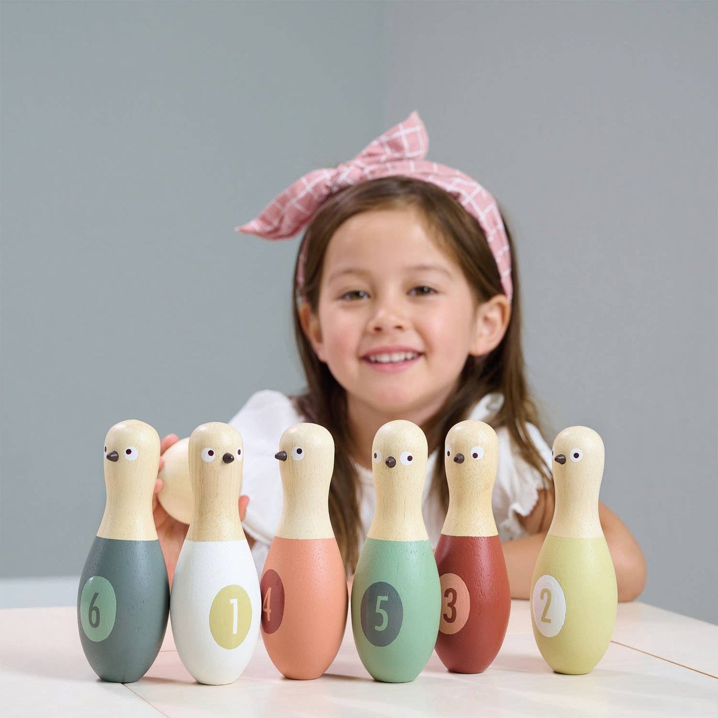 Child with a set of colorful wooden bowling pins on a plain background