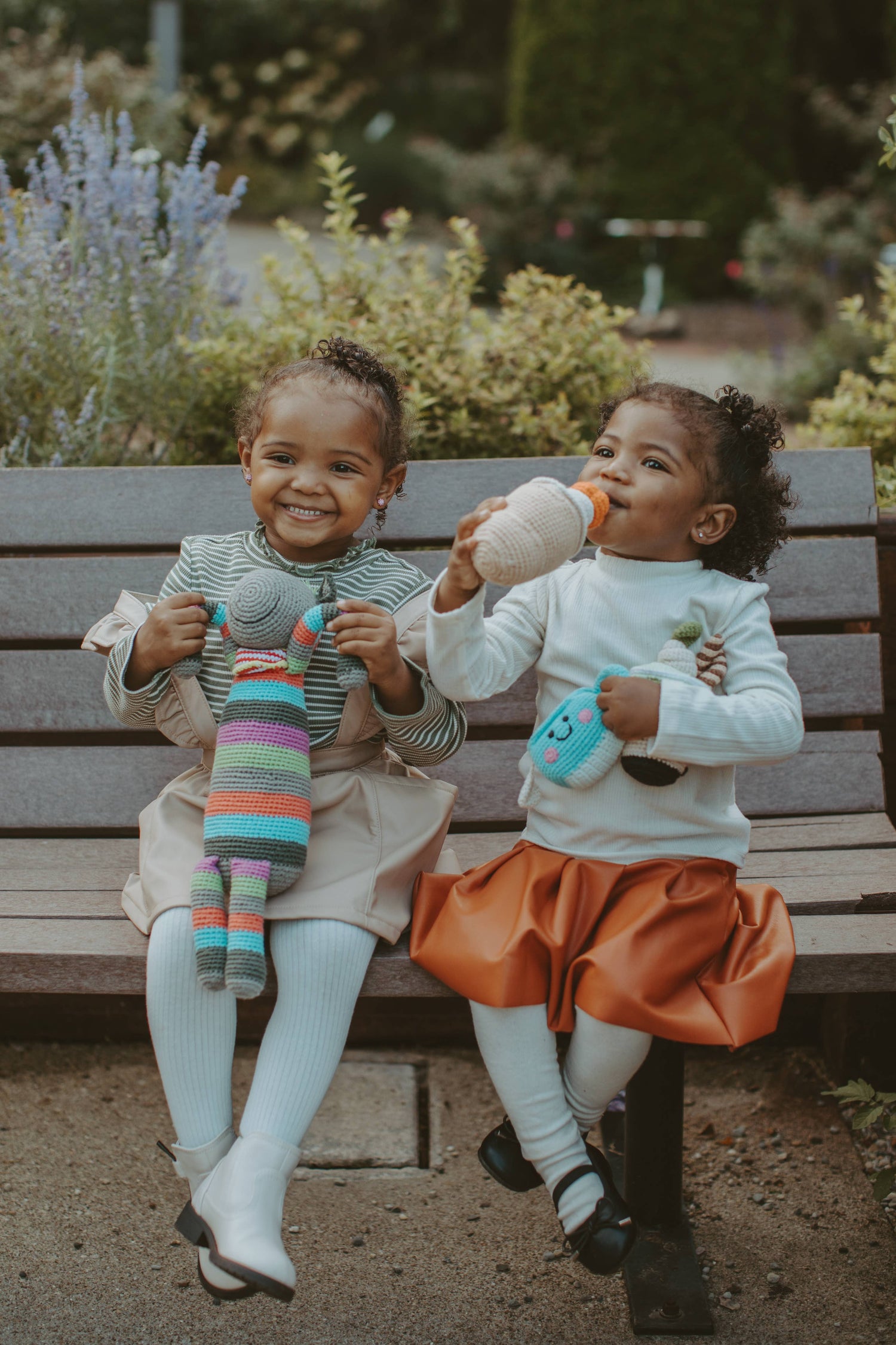 two girls sitting on a park bench playing with knitted toys