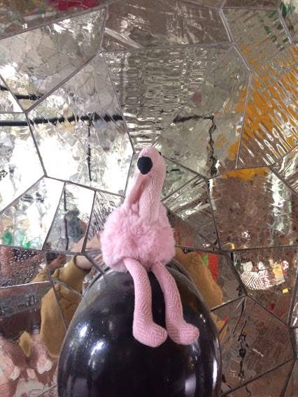 Pink flamingo toy on a black bottle against a reflective mirror background