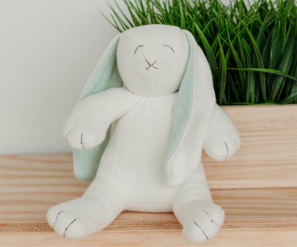 White plush bunny toy with green ears on a wooden surface with grass in the background