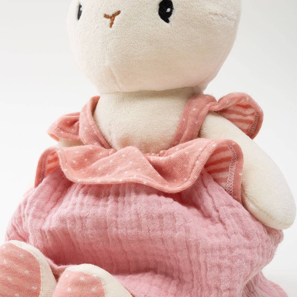 Stuffed animal toy wearing a pink dress with ruffled collar on a white background