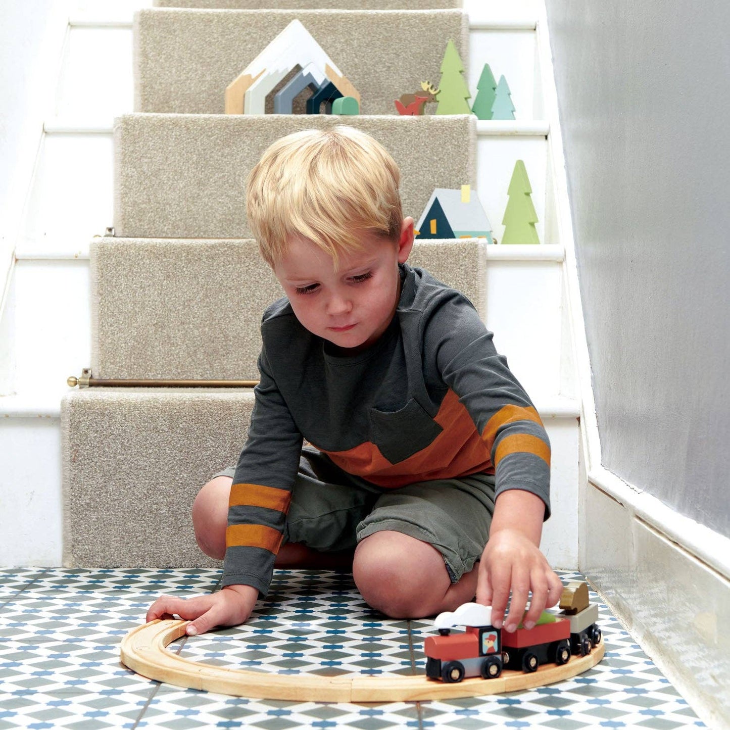 Child playing with a wooden train set on a patterned rug.