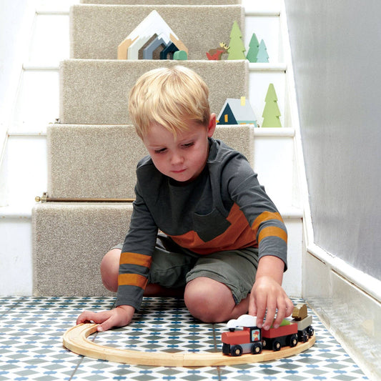Child playing with a wooden train set on a patterned rug.