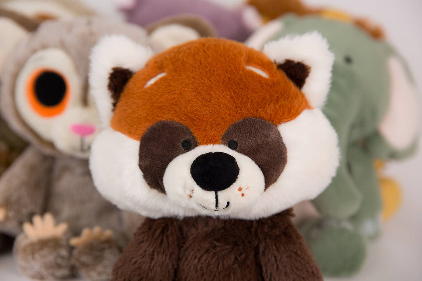 Close-up of a plush red panda toy with other plush toys in the background.