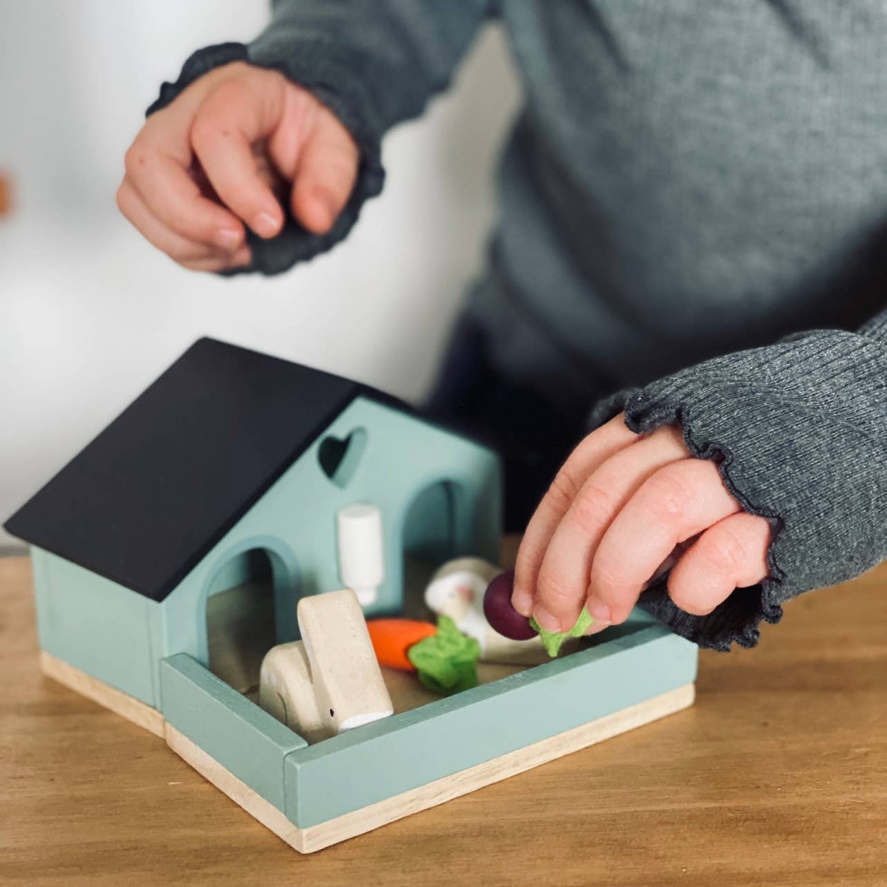 Child playing with a small toy house and vegetables on a wooden surface