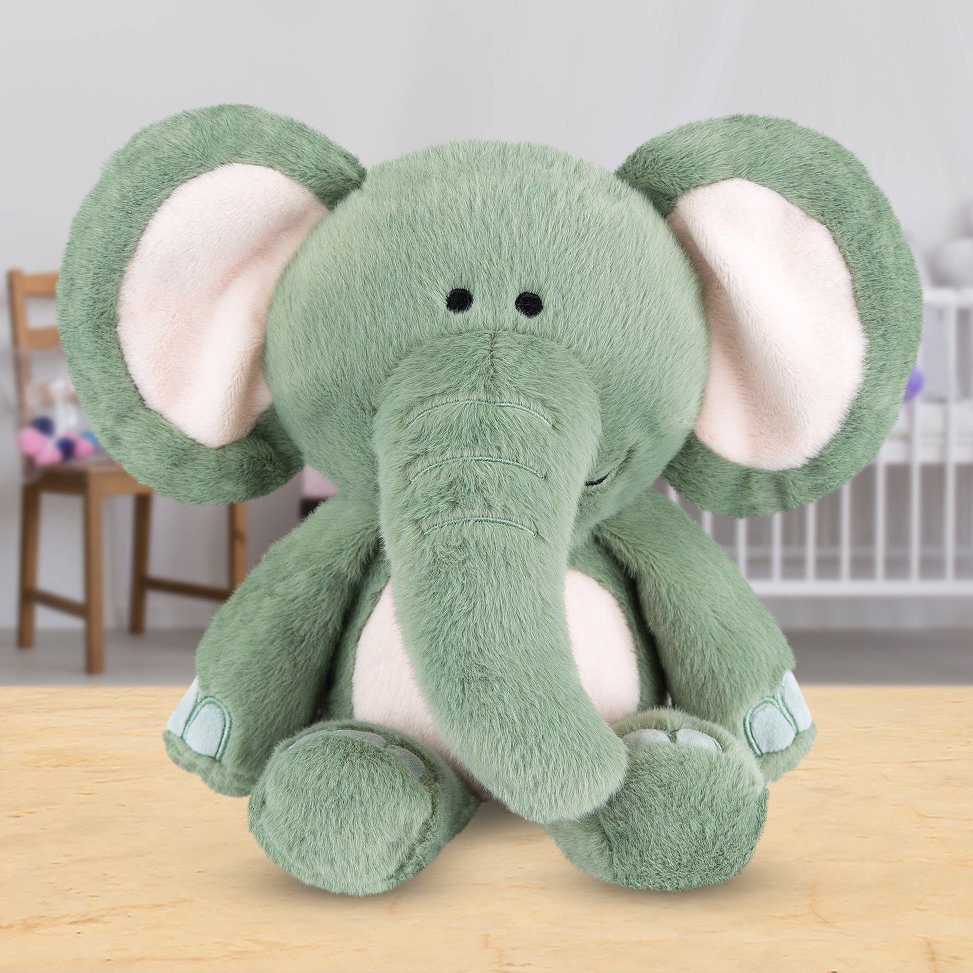 Grey plush elephant toy on a wooden surface with a blurred background