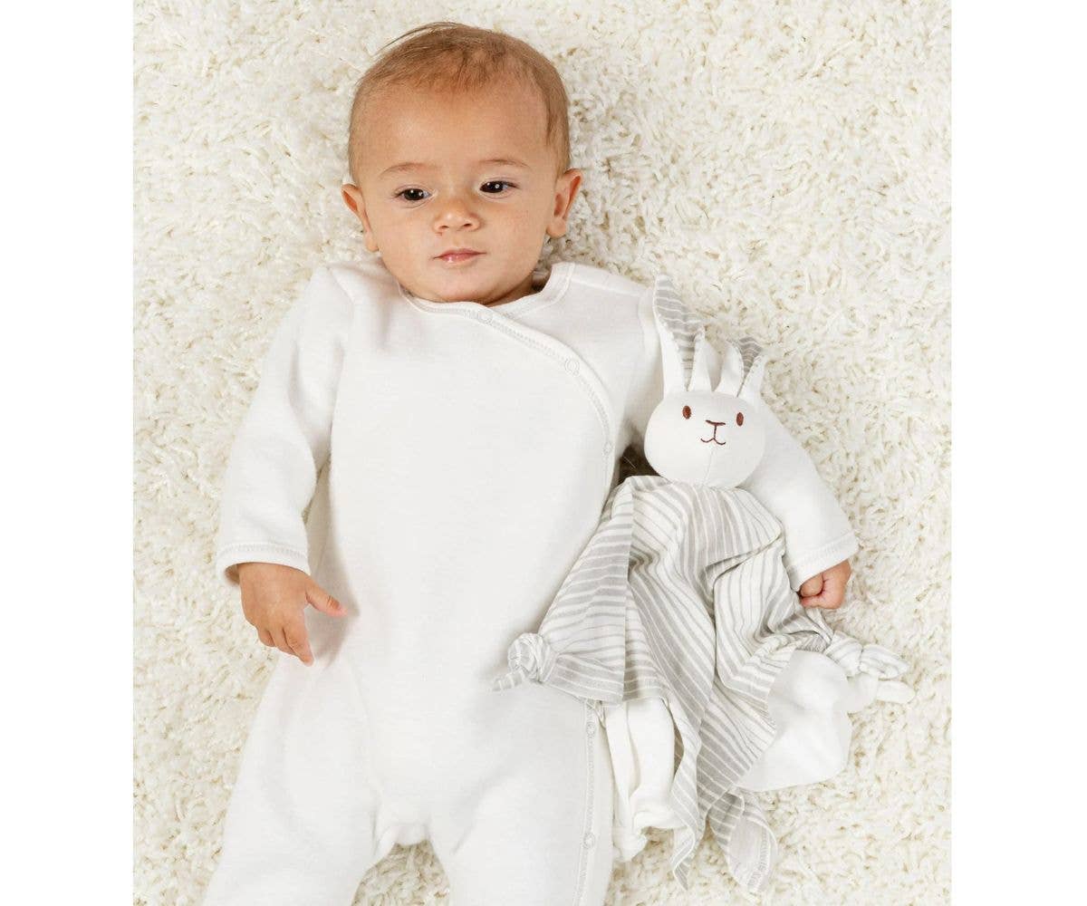 Baby in a white outfit holding a soft toy on a white background