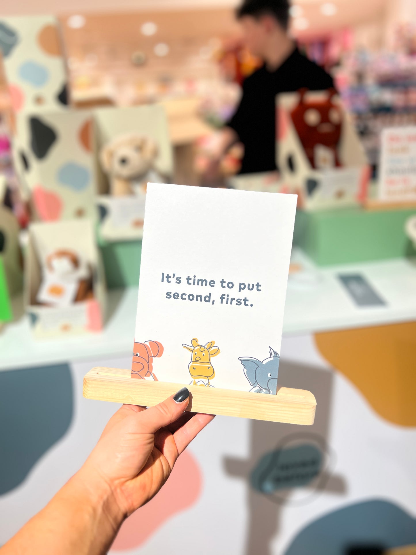 Hand holding a card with cartoon characters and text in a store setting
