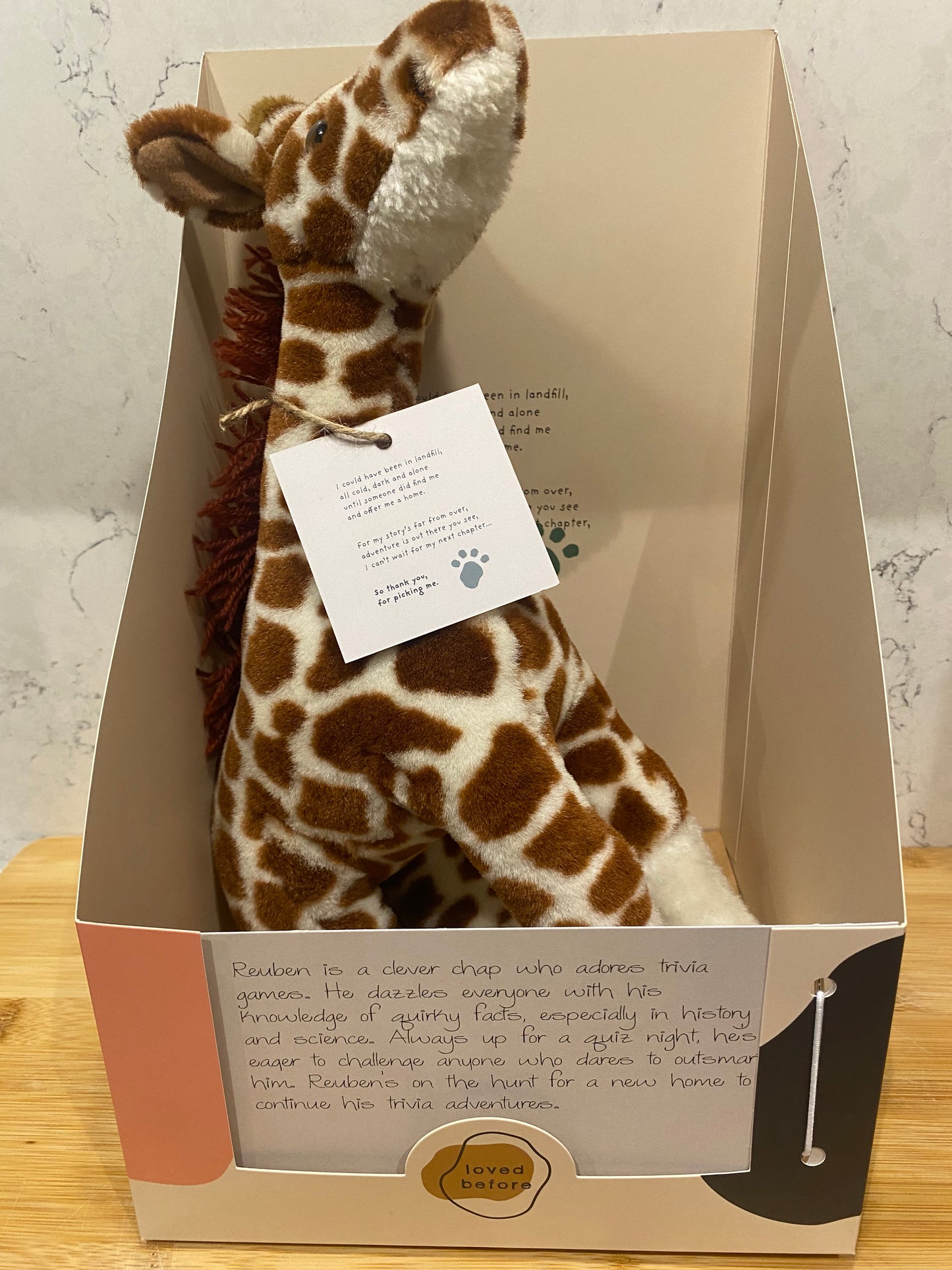 Plush giraffe toy in a gift box with a card on a textured surface