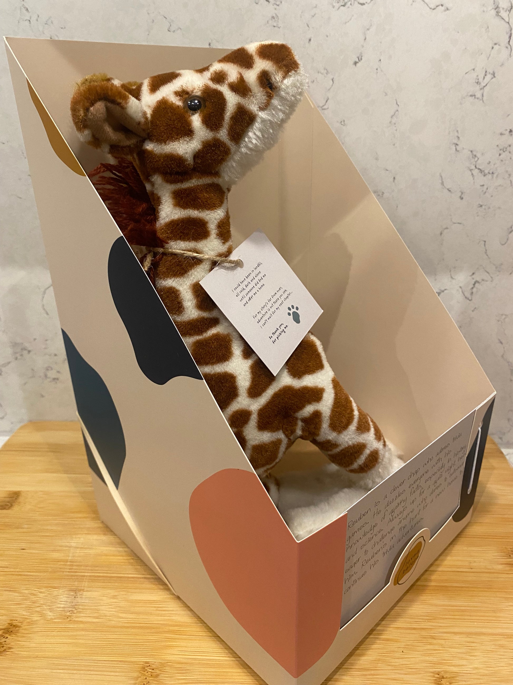 Plush giraffe toy in a decorative box on a marble surface