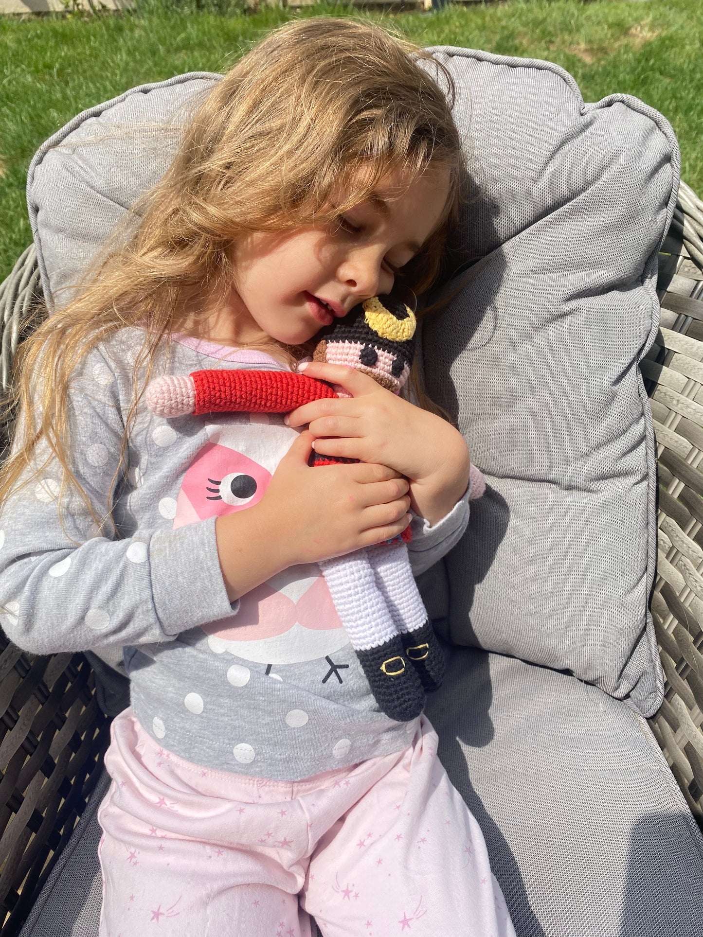 Child lying on a cushioned chair holding a knitted nutcracker doll outdoors