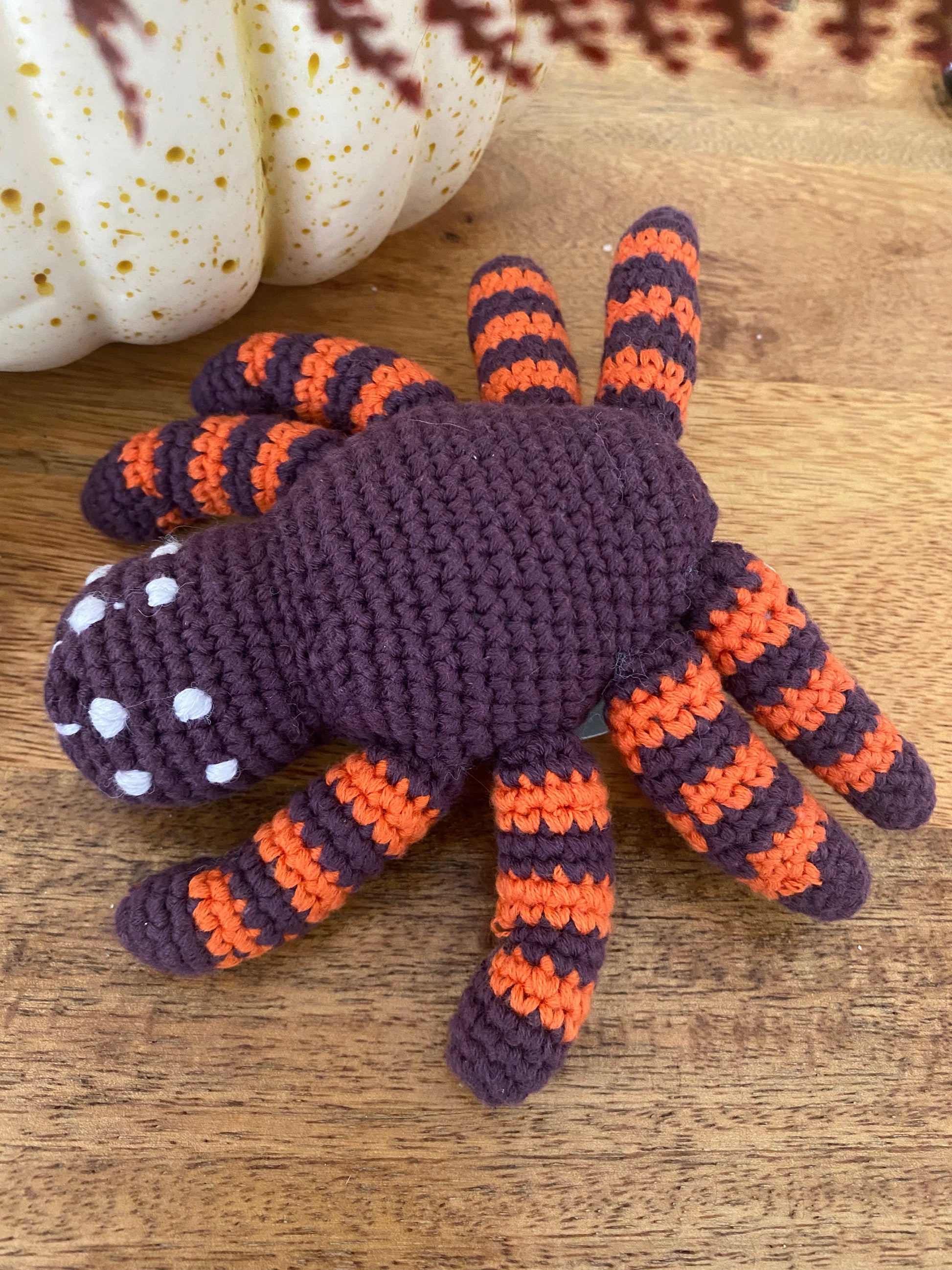 Crocheted spider toy with orange and purple stripes on a wooden surface