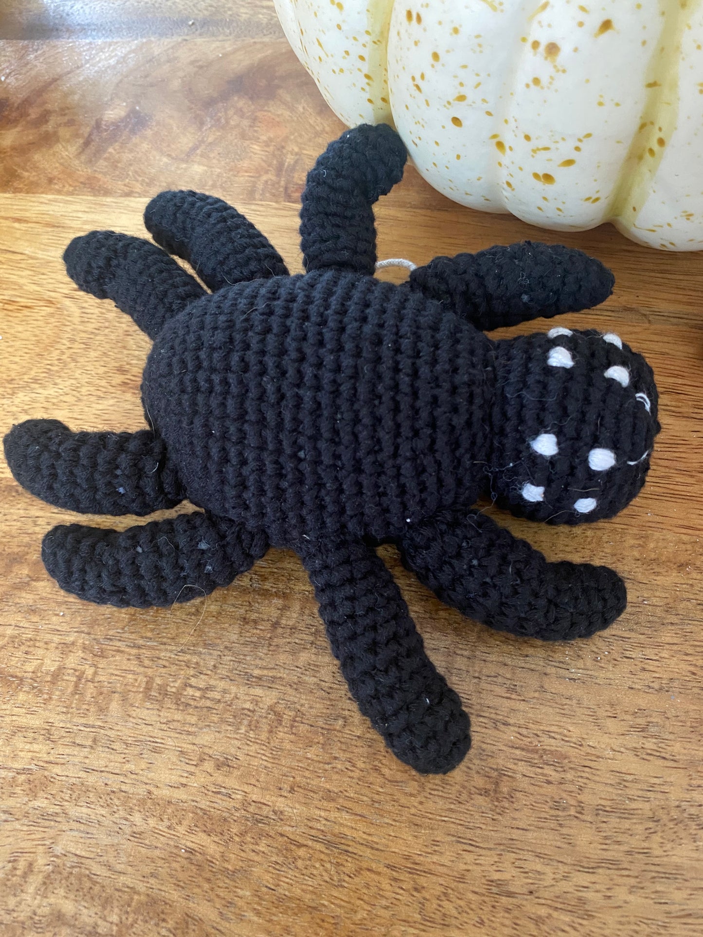 Black crocheted spider toy on a wooden surface with white marbled objects.