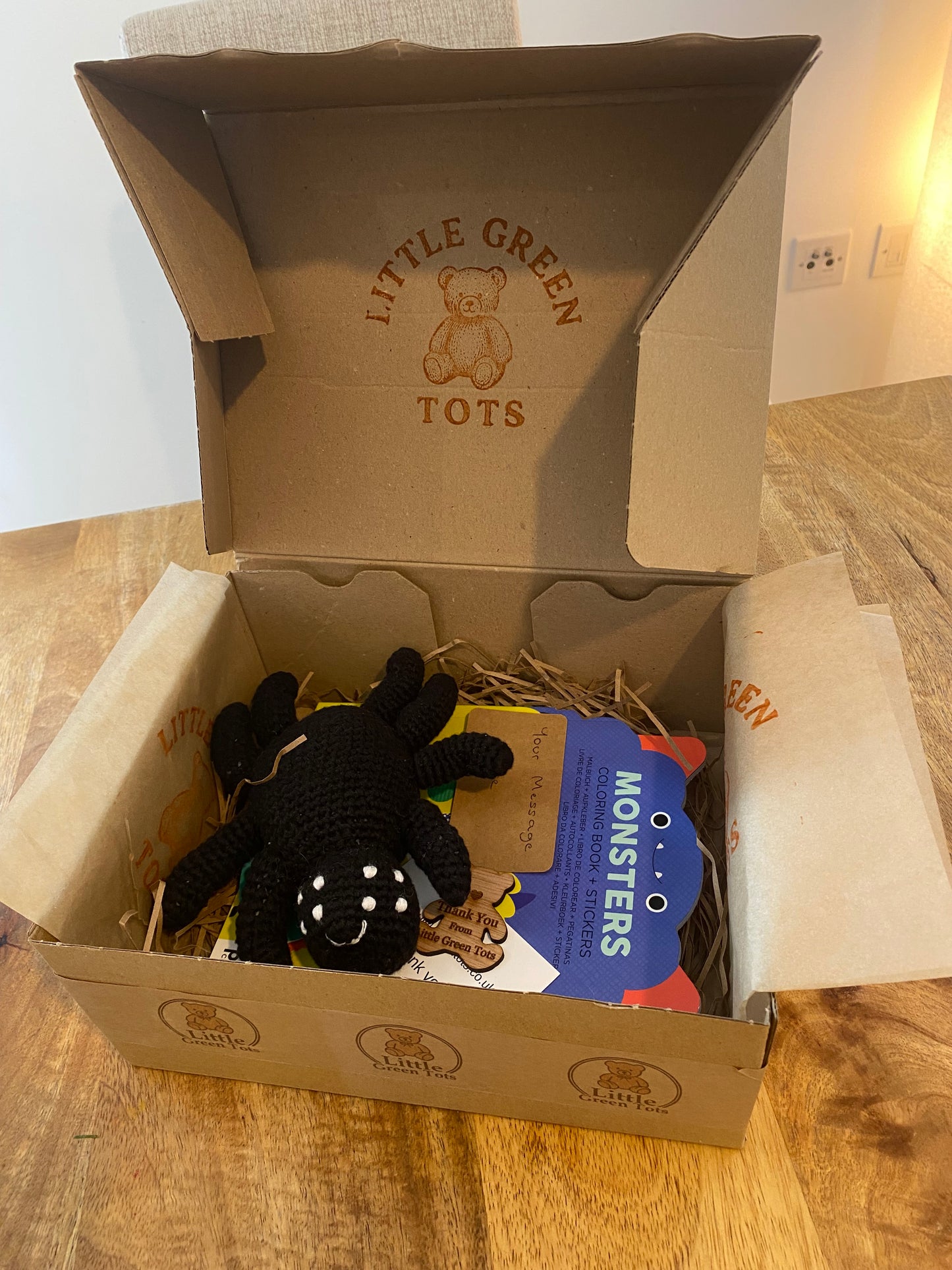 Open cardboard box with Little Green Tots branding, containing a plush toy and coloring book.