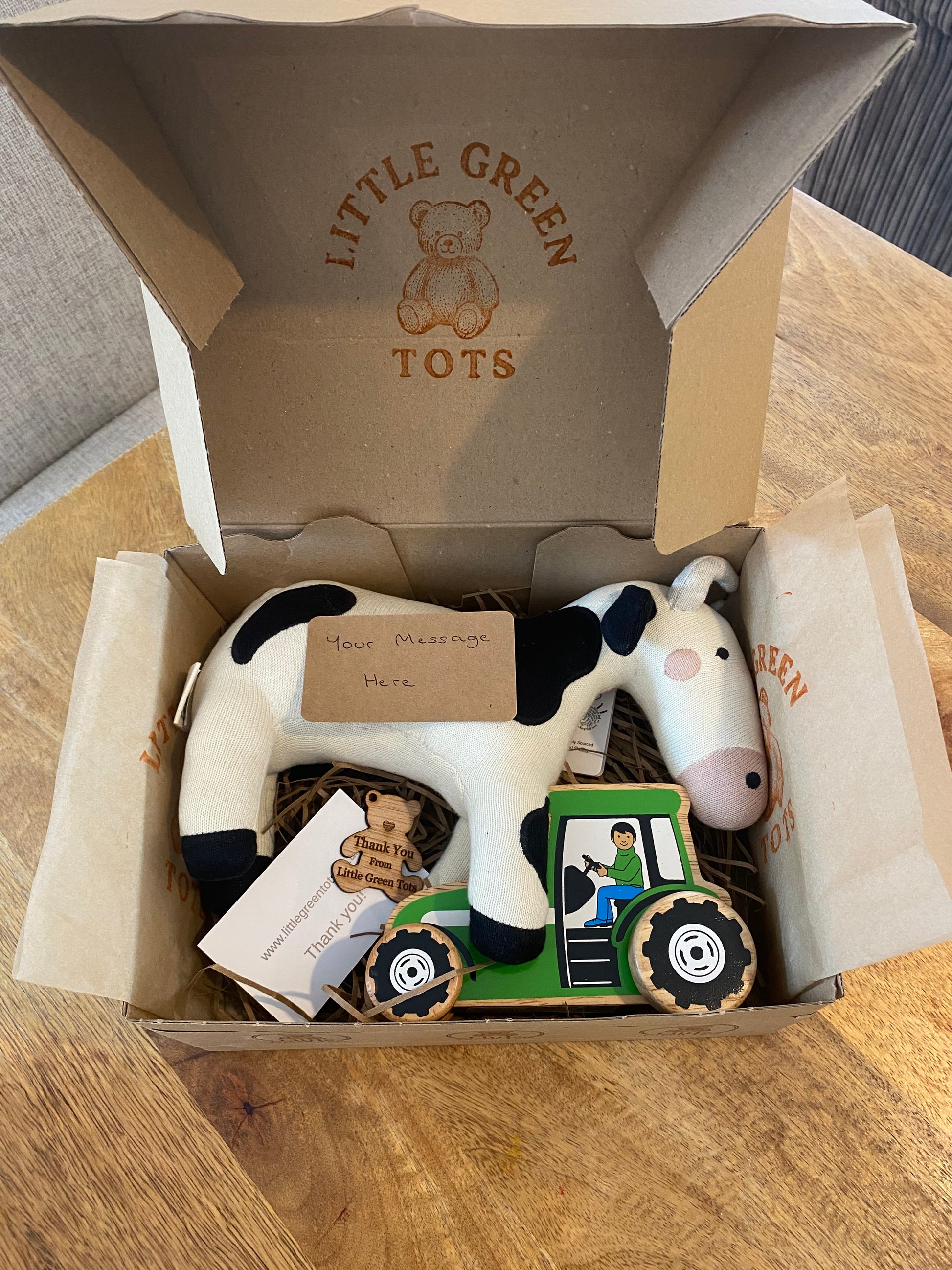 Open cardboard box with toys and a cow plushie on a wooden surface