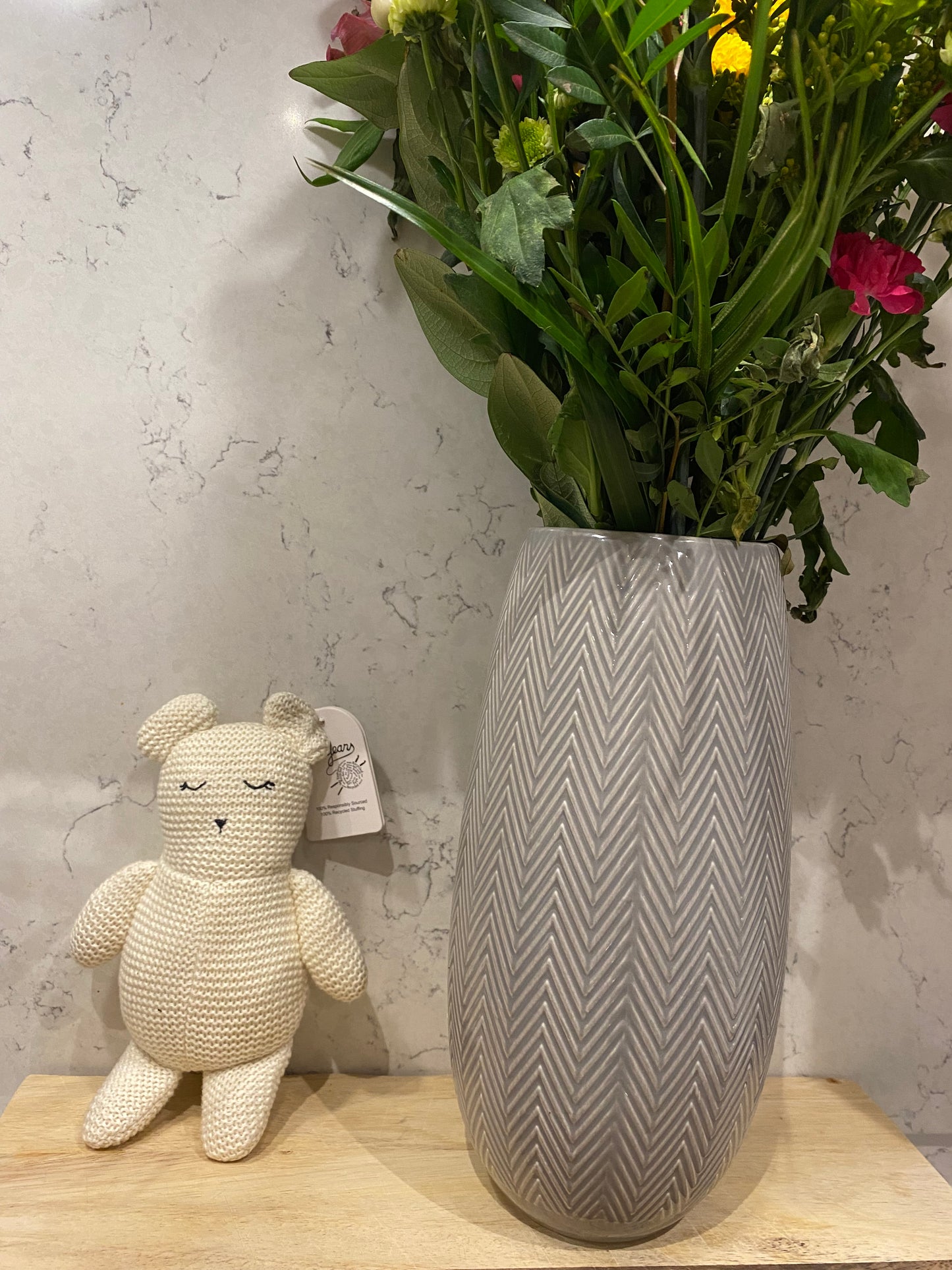 Gray textured stool with a small white plush toy on a light-colored surface next to a bouquet of flowers.