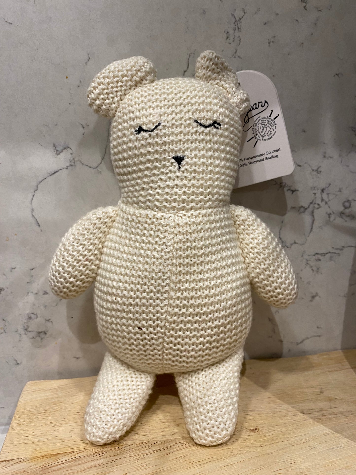 Knitted teddy bear toy on a marble surface with a wooden block underneath