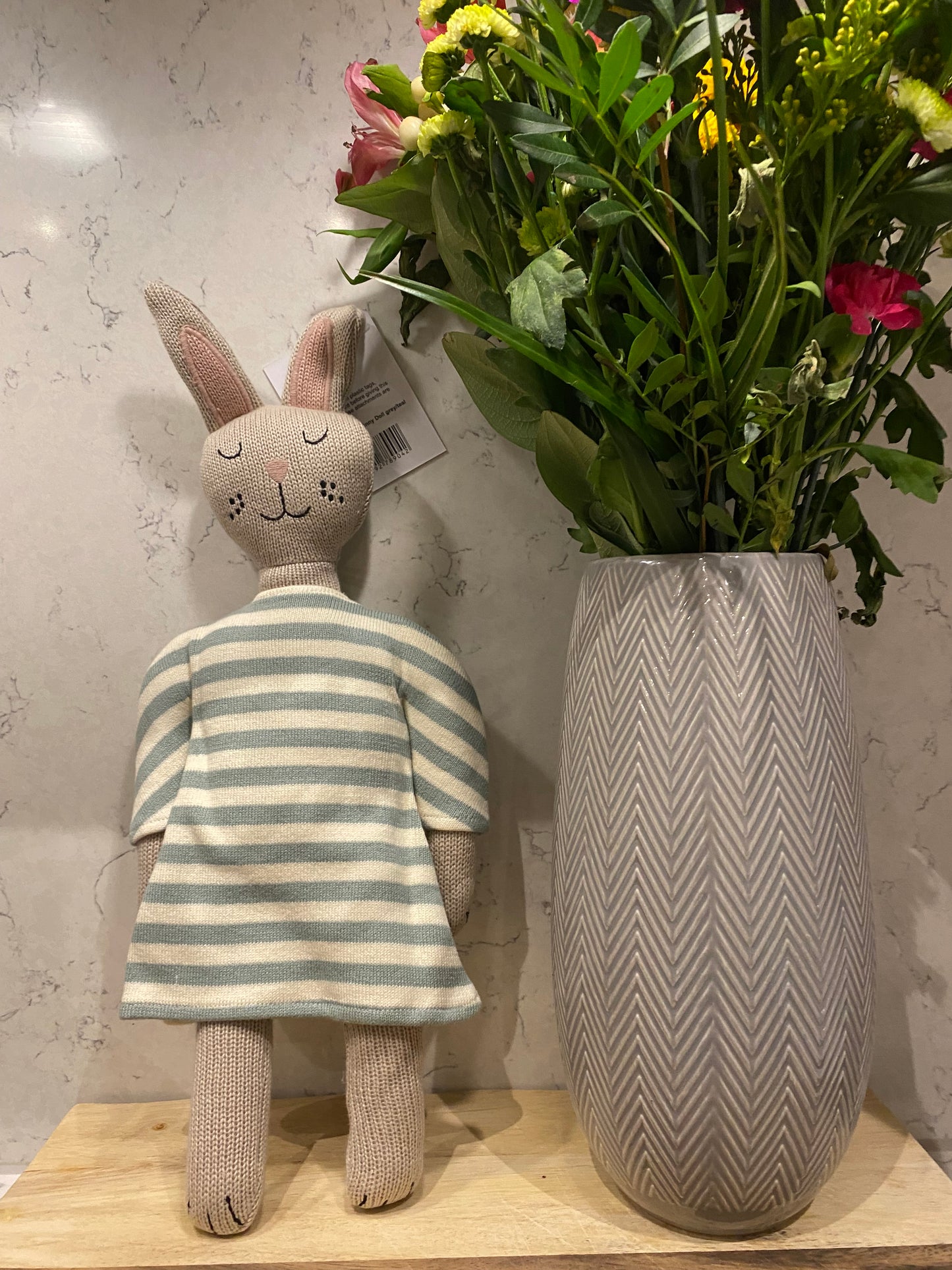Floral arrangement next to a plush toy with a striped dress on a marble surface.