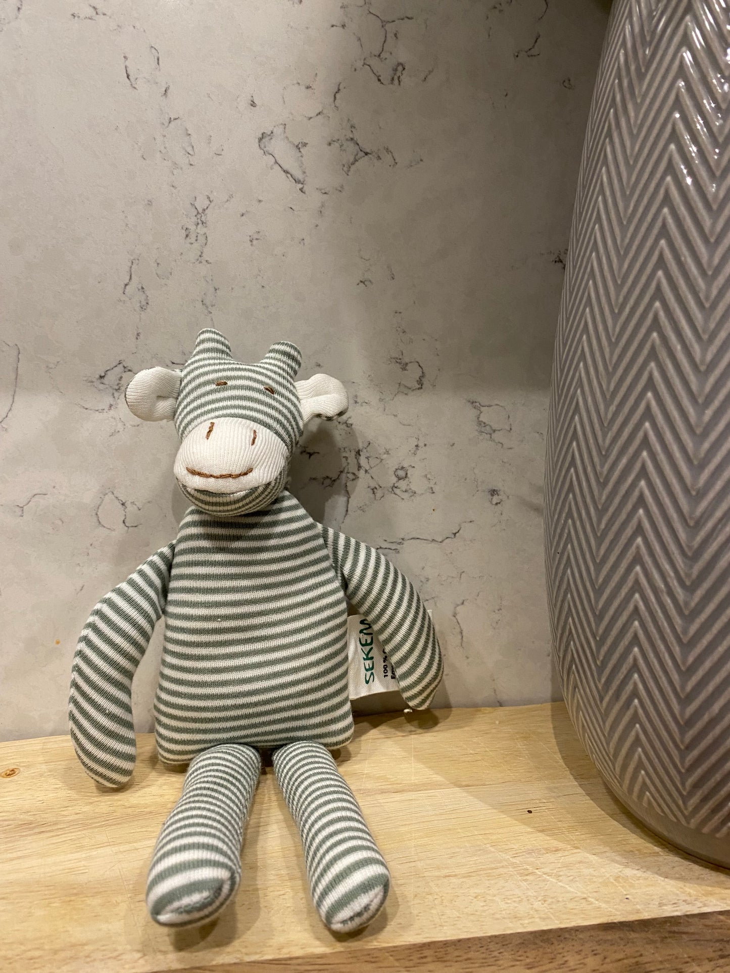 Striped toy giraffe on a wooden surface with a textured wall background