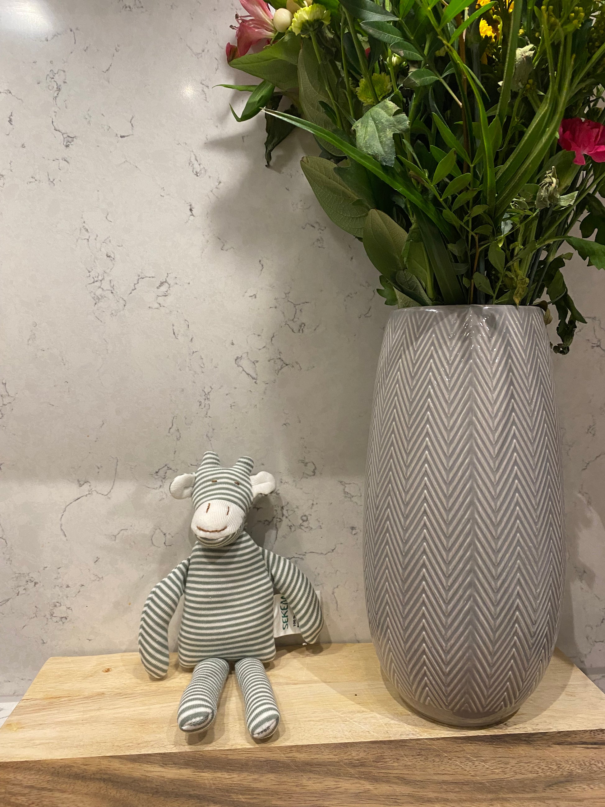 Gray striped giraffe toy on a wooden surface with flowers in the background