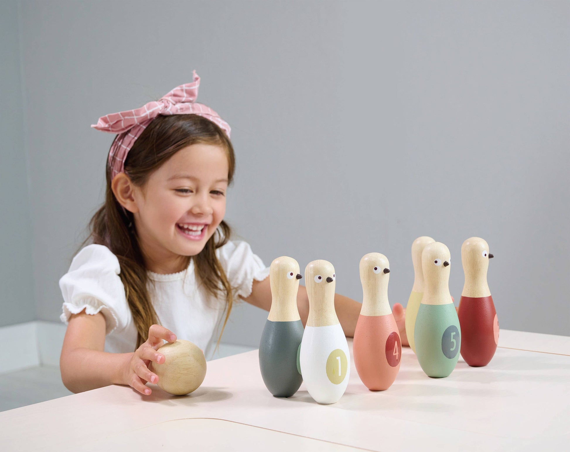 Child playing with colorful wooden bowling pins on a table